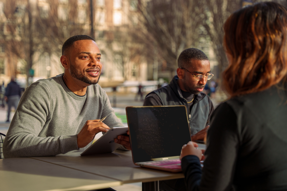 two people using laptops sitting at a table together on Tech campus